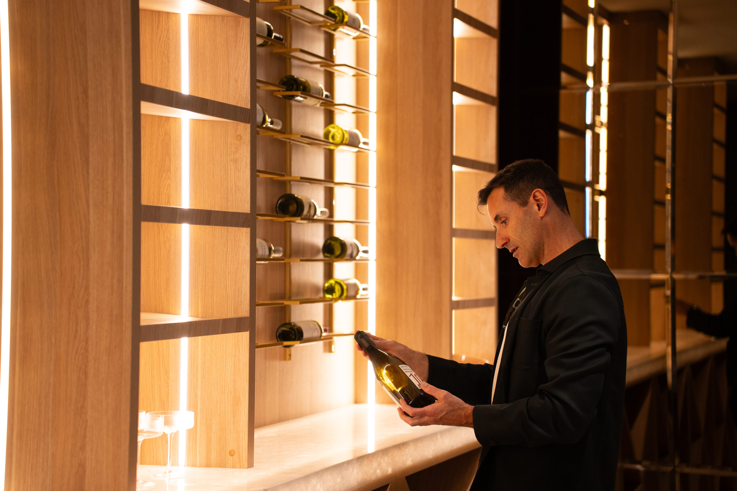 A man who is a buyer agent is holding a bottle of wine inside a home in Brighton Melbourne